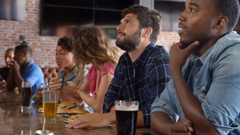 Grupo-de-amigos-viendo-el-juego-en-el-Bar-de-deportes-en-pantallas