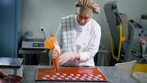 Pastelería-con-jeringa-de-repostería-hace-galletas-del-mismo-tamaño-antes-de-hornear-en-la-cocina.-Postres-crudos-en-cubierta.-Herramientas-de-la-cocina-para-cocinar-dulces.-Ayudante-cocinero-recipiente-de-crema