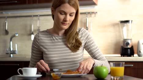 Hermosa-joven-haciendo-pan-y-mantequilla-con-mermelada.-Desayuno-con-zumo-y-café-en-la-cocina