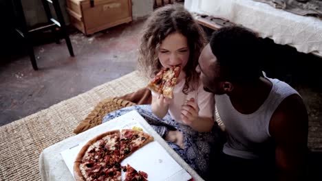 Woman-offers-pizza-to-man,-but-eat-slice-by-herself.-Multiracial-couple-having-fun-during-the-meal-with-fast-food