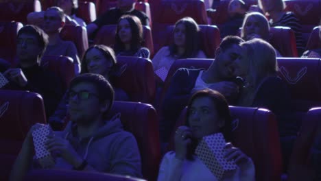 Young-romantic-couple-is-making-out-and-kissing-while-watching-a-film-screening-in-a-movie-cinema-theater.