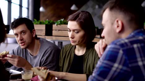 Una-mujer-bonita-tiene-un-sándwich-de-atún,-verdes-y-tomates-en-una-compañía-de-amigos,-hablando-emocionalmente-las-últimas-noticias-y-disfrutar-de-una-agradable-comida