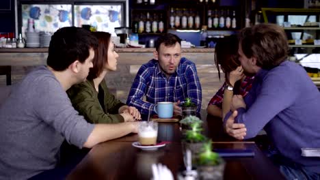 Friends-sitting-at-the-table-in-cafe-enjoying-leisure-time-together-talking-to-each-other.-Students-chatting-while-having-lunch-at-the-restaurant.-People-drinking-beverages-and-having-conversation