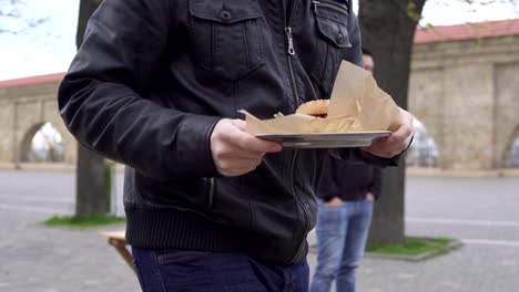 Hombre-joven-en-un-café-de-calle-pisando-gran-placa,-sentarse-a-su-mesa-con-sabrosa-hamburguesa.-Él-se-va-a-comer.-Rodada-en-4k