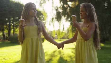 Two-Girls-are-Walking-at-Park-and-Holding-Ice-Cream-in-Hands