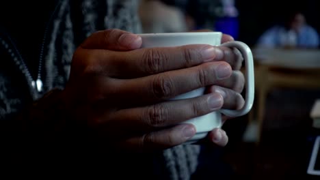 Mano-de-mujer-sosteniendo-una-taza-de-café-en-la-cafetería-en-el-día-de-lluvia