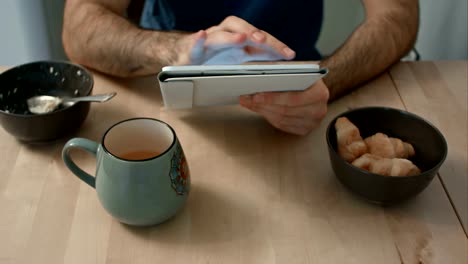 Man's-hands-holding-digital-tablet-at-breakfast-table