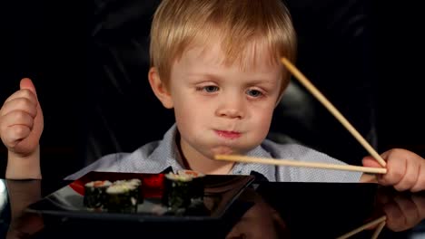 Caucasian-boy-is-eating-sushi-on-black-background.