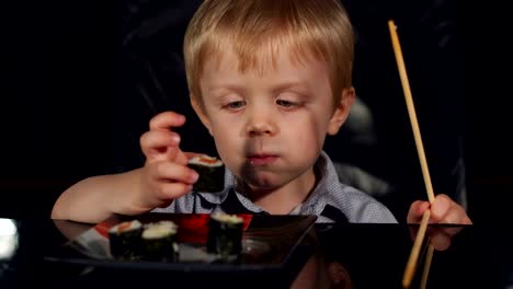 Close-up-of-child-eating-sushi-on-black-background