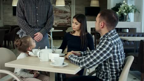 Young-family-with-daughter-having-dinner-at-restaurant.-Father-call-waiter-so-that-his-wife-make-order