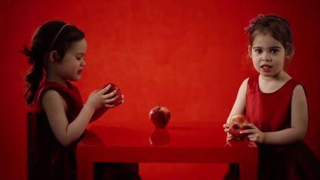 Two-little-girls-eat-apples-on-a-red-table