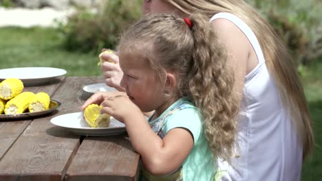 Family-having-lunch-in-the-garden-eating-boiled-corn-on-the-cob