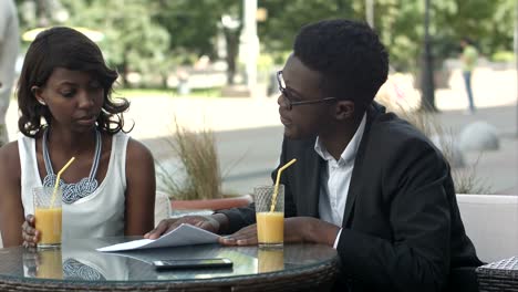 African-american-business-people-holding-papers,-explaining-details-while-having-a-meeting-at-a-coffee-shop