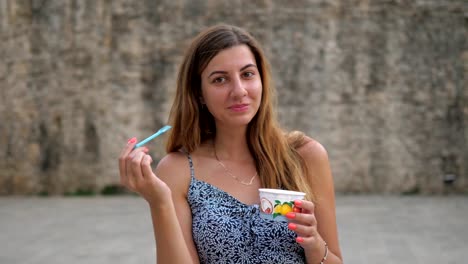 Süße-junge-Frau,-die-mit-einem-Löffel-aus-einem-Becher-Eis-auf-der-Straße-Essen