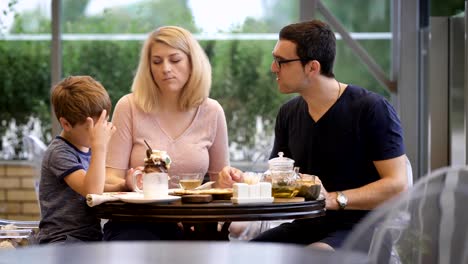 Mom-looks-at-her-son-and-eats-a-pizza,-the-child-fools-around-with-his-family,-the-father-sits-next-to-him-and-watches-his-relatives