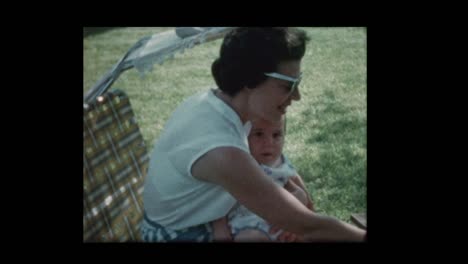 Mom-feeds-baby-sitting-outside-on-lawn-chair-1960