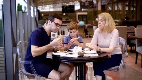 Una-familia-feliz-come-en-un-restaurante,-un-esposo-y-una-esposa-ordenaron-una-pizza,-su-pequeño-hijo-se-complace-con-la-opción-deliciosa-de-sus-padres