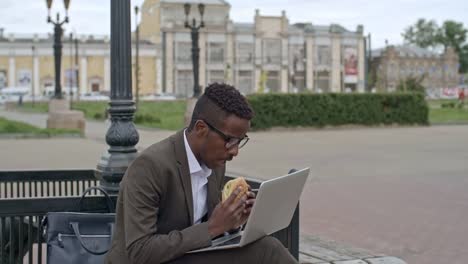 Geschäftsmann-mit-Laptop-im-Freien-und-essen-Burger