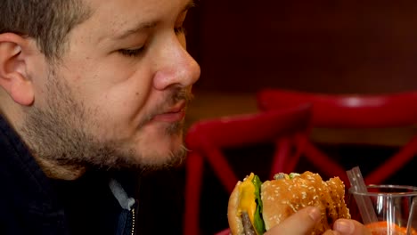 Hungry-man-bytes-a-big-burger.Close-up-on-man-eating-burger