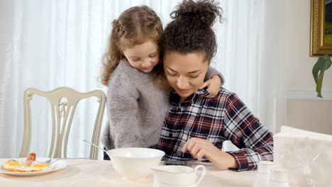 Cute-little-girl-embrace-her-mother-and-looks-with-her-something-on-a-smartphone