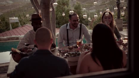 Young-multi-ethnic-friends-eating-mediterranean-lunch-on-rustic-cottage-patio