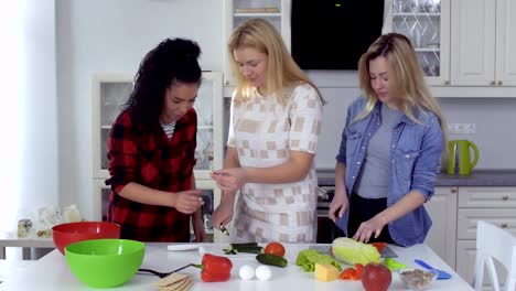 Curly-brunette-comes-to-her-friends-at-the-kitchen-and-tries-cucumber-for-salad