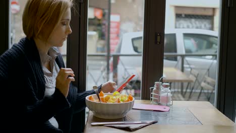 schöne-Frau-mit-ihrem-Handy-in-der-Mittagspause-beim-Essen-eines-Salats