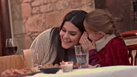 Young-daughter-whispering-secrets-in-mother's-ear-at-lunch