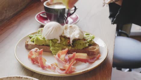 Frau-drückte-Zitrone-über-pochiertem-Ei-und-Avocado-auf-Toast