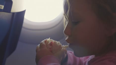 Close-up-child-girl-eat-burger-with-appetite-over-porthole-in-airplane