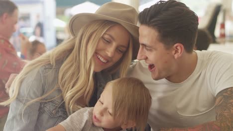 Young-loving-couple-gaze-into-each-others-eyes,-while-their-son-eats-curly-fries-at-an-outdoor-food-court