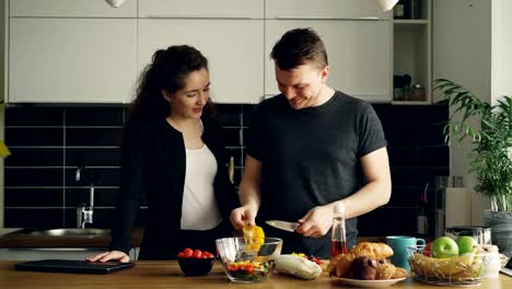 junge-schöne-kaukasischen-ziemlich-lockig-Geschäftsfrau-nach-Hause-kam-von-der-Arbeit,-ihr-hübscher-Mann-kocht,-gelbe-Paprika-schneiden,-sie-küssen-und-lachen