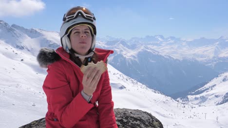 Esquiador-de-la-mujer-se-sienta-en-una-piedra-en-el-centro-de-esquí-de-las-montañas-y-come-un-sándwich