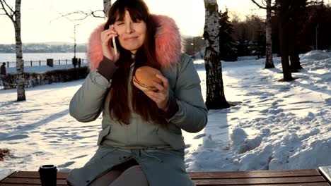 Junge-Frau-isst-einen-Burger-auf-Winter-Straße