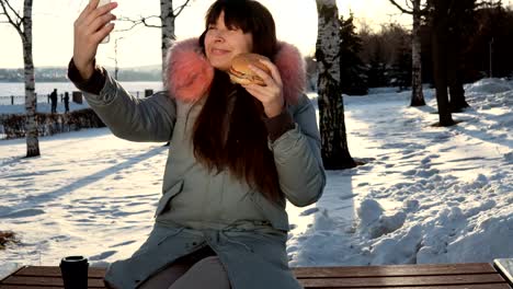 Young-woman-eats-a-burger-on-winter-street