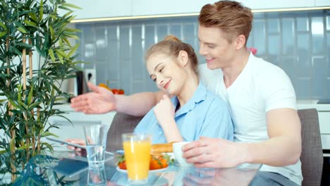 Pareja-joven-con-tableta-digital-desayunando-en-la-mesa-de-la-cocina.