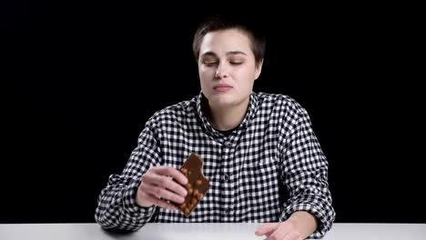 Young-unordinary-girl-is-eating-bar-of-chocolate,-diet-conception,-black-background