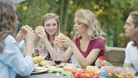 Freunde-Essen-Burger-sitzen-am-Esstisch-auf-Outdoor-Party