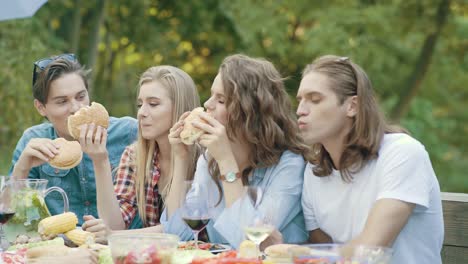 Freunde-Essen-Burger-sitzen-am-Esstisch-auf-Outdoor-Party