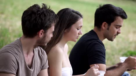 Three-Happy-Young-Friends-Eating-On-Picnic