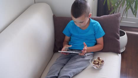 Handsome-boy-sitting-on-couch-and-using-tablet-at-home