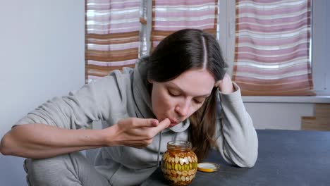 Woman-dips-her-finger-in-honey-with-nuts-in-the-jar.-Eats-honey-from-finger.