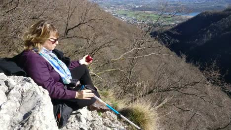 Frau-mit-blonden-Haaren-ist-ausruhen-und-Essen-eines-Apfels-an-der-Spitze-eines-hohen-Berges