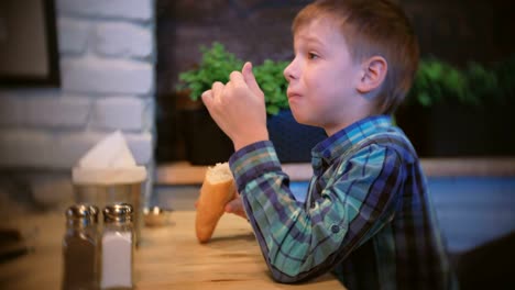 Niño-come-una-baguette-y-relojes-TV-en-la-cafetería.-Vista-lateral.