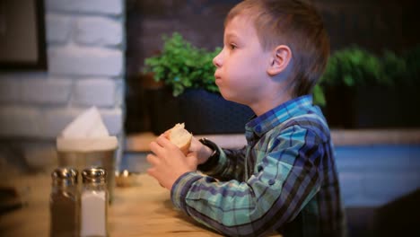 Boy-eats-a-baguette-and-watches-TV-in-the-cafe.-Side-view.