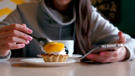 Mujer-irreconocible-come-una-torta-con-una-cuchara-y-mira-la-pantalla-del-teléfono.-De-cerca.