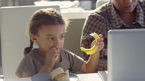 Girl-Snacking-while-Spending-Time-with-Working-Mother