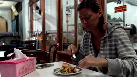 Woman-eating-a-hamburger-in-a-cafe-with-a-fork-and-knife