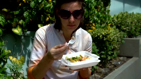 Streetfood.-Eine-Frau-sitzt-auf-der-Straße-auf-einer-Brüstung,-gedünstetem-Gemüse-aus-einem-Container-Essen