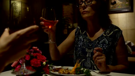 Women-sitting-at-a-table-in-a-restaurant,-eating,-talking,-clink-glasses-and-drink-red-wine